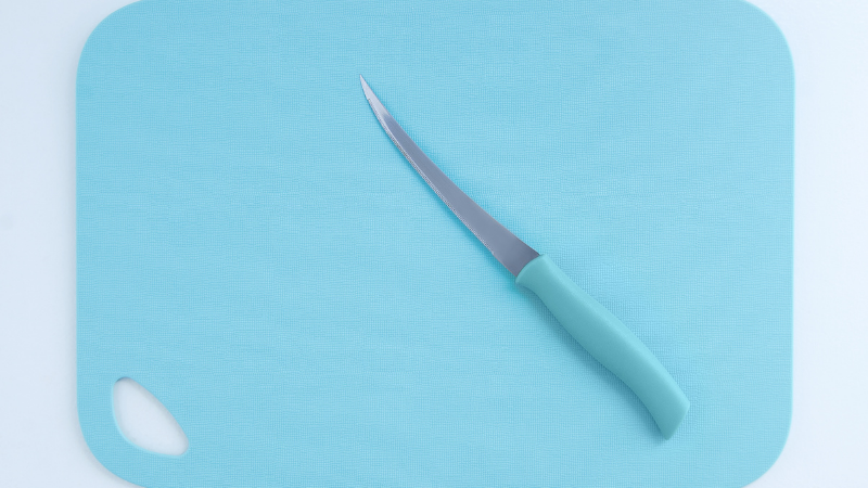 Kitchen knife resting on a blue chopping board on a preparation surface.